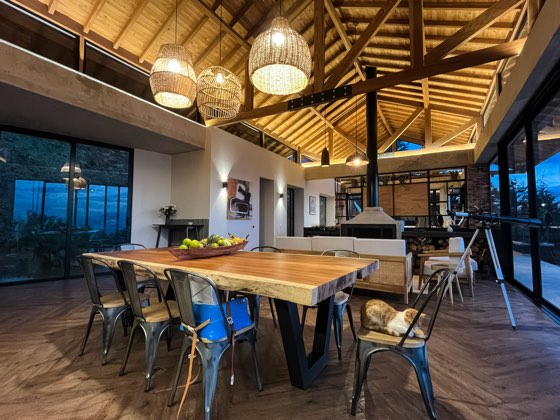Gran mesa de comedor en madera maciza bajo lámparas de ratán
