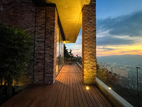 Corredor de madera con pilares de ladrillo y atardecer sobre la ciudad