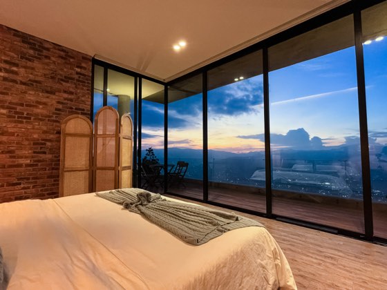 Suite principal con cama frente a ventanales y crepúsculo sobre Medellín