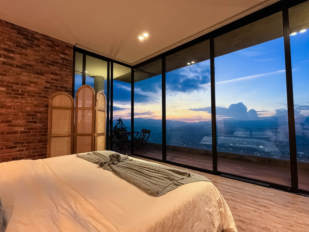 Suite principal con cama frente a ventanales con vista al atardecer sobre Medellín