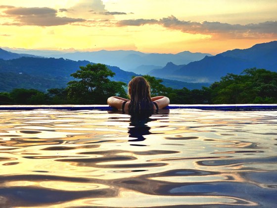 Bañista en el borde infinito de la piscina al atardecer